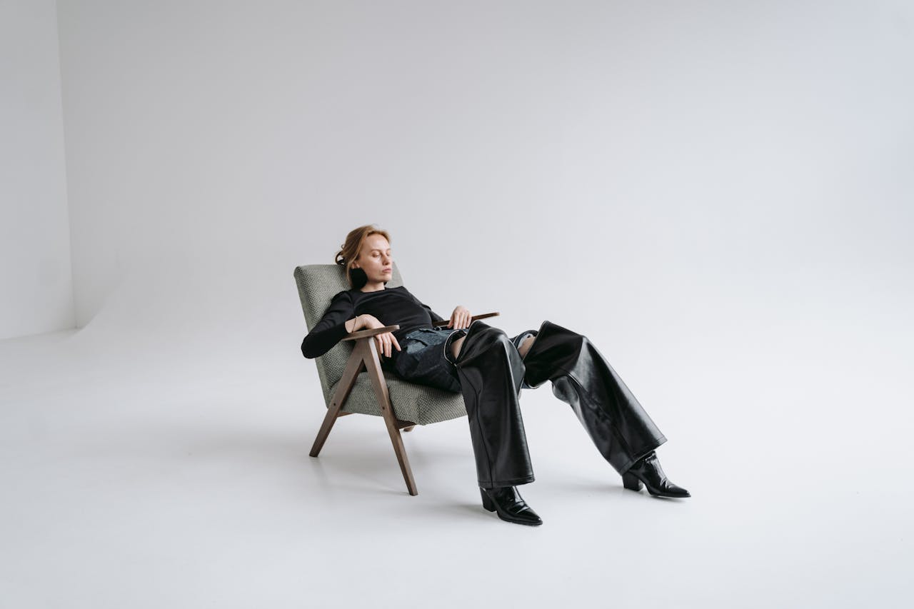 Stylish woman in black leather outfit reclines in a minimalist studio with open space.